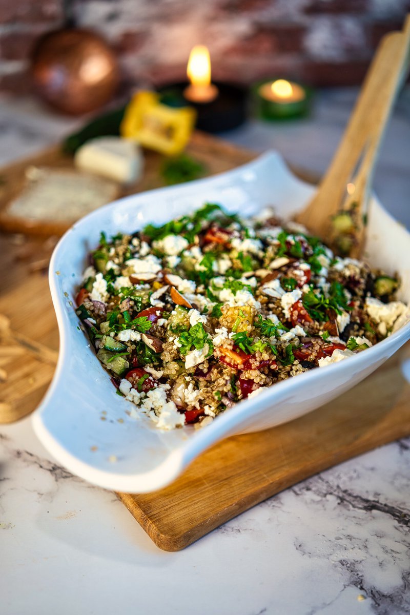 Quinoa salad with vegetables and feta cheese served in a decorative white bowl, with a wooden spoon.