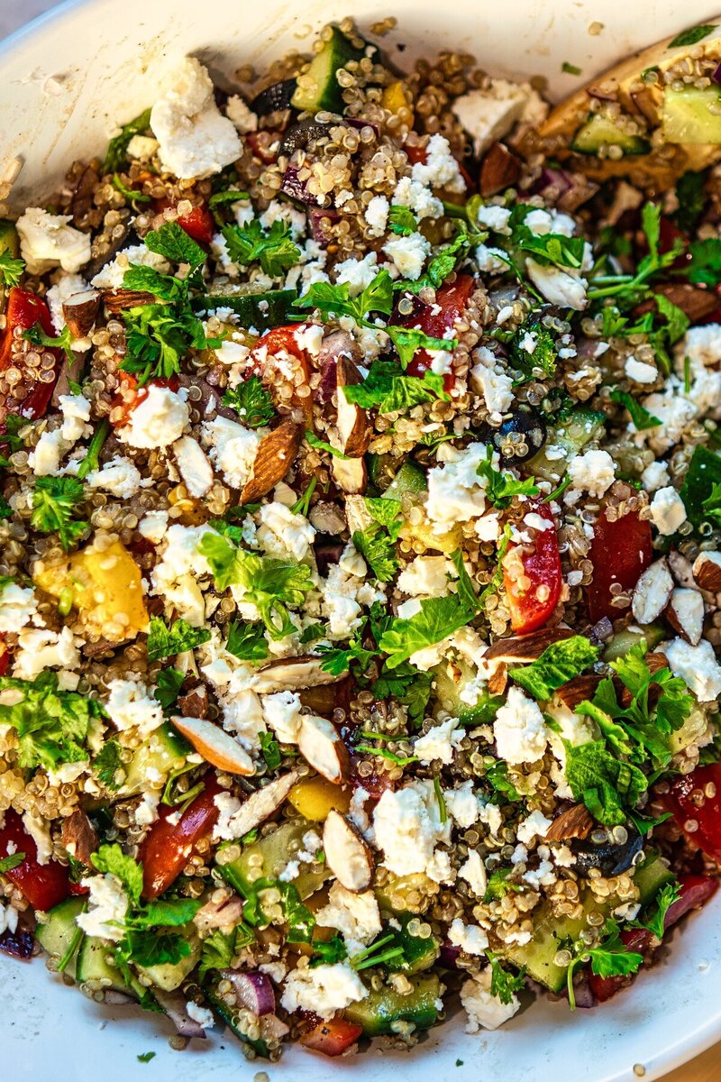 Overhead close up view of quinoa salad featuring tomatoes, cucumber, nuts, cheese, and fresh herbs.