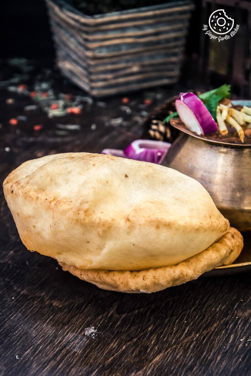 there is a plate with a puffed up bhature and a bowl of chole