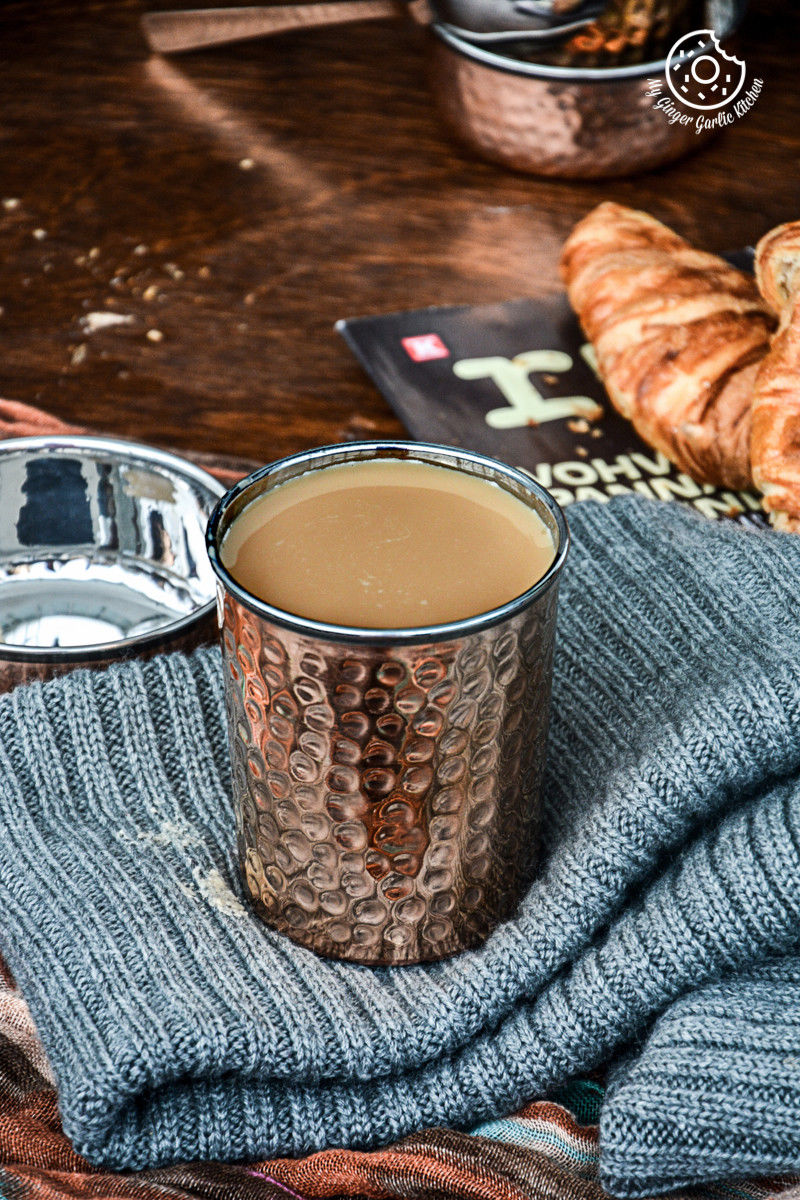 there is a cup of spiced kesar chai and a croissant on a table