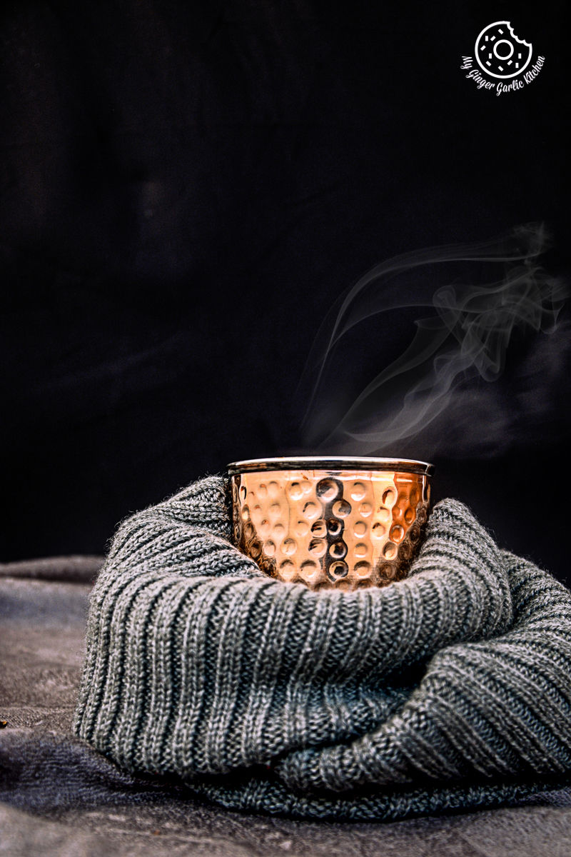 there is a cup of hot spiced kesar chai topped with saffron strands on a scarf on a table