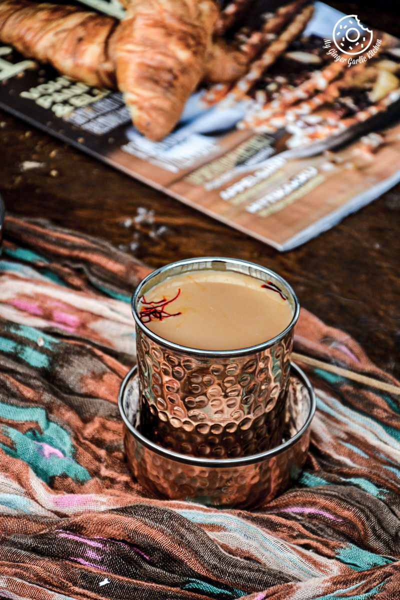 there is a cup of spiced kesar chai topped with saffron strands and a croissant on a table
