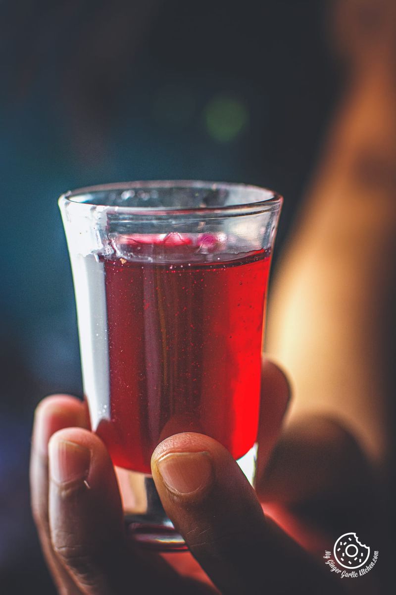 a hand holding homemade rose syrup small glass