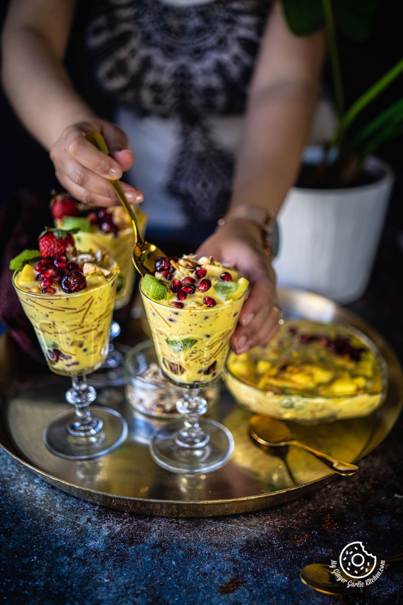 a female holding a golden spoon over a vermicelli fruit custard glass
