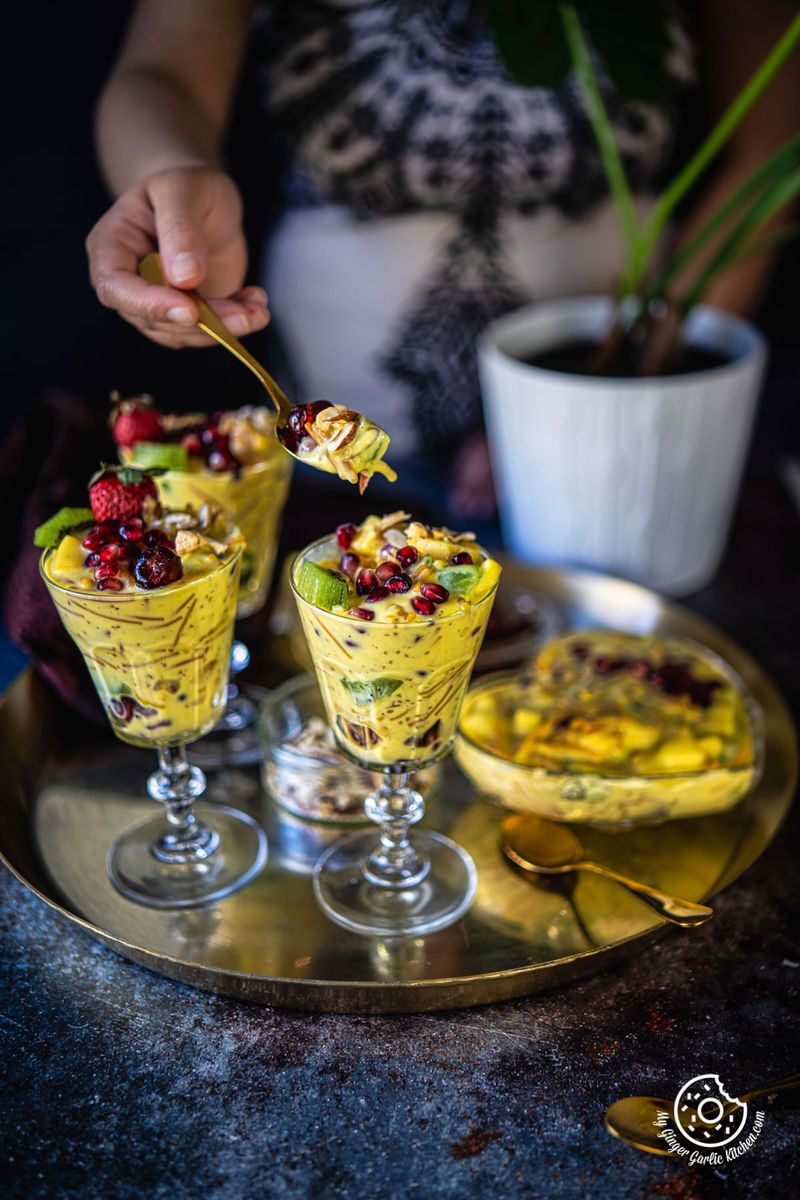 a female holding a golden spoon filled with custard over a vermicelli fruit custard glass