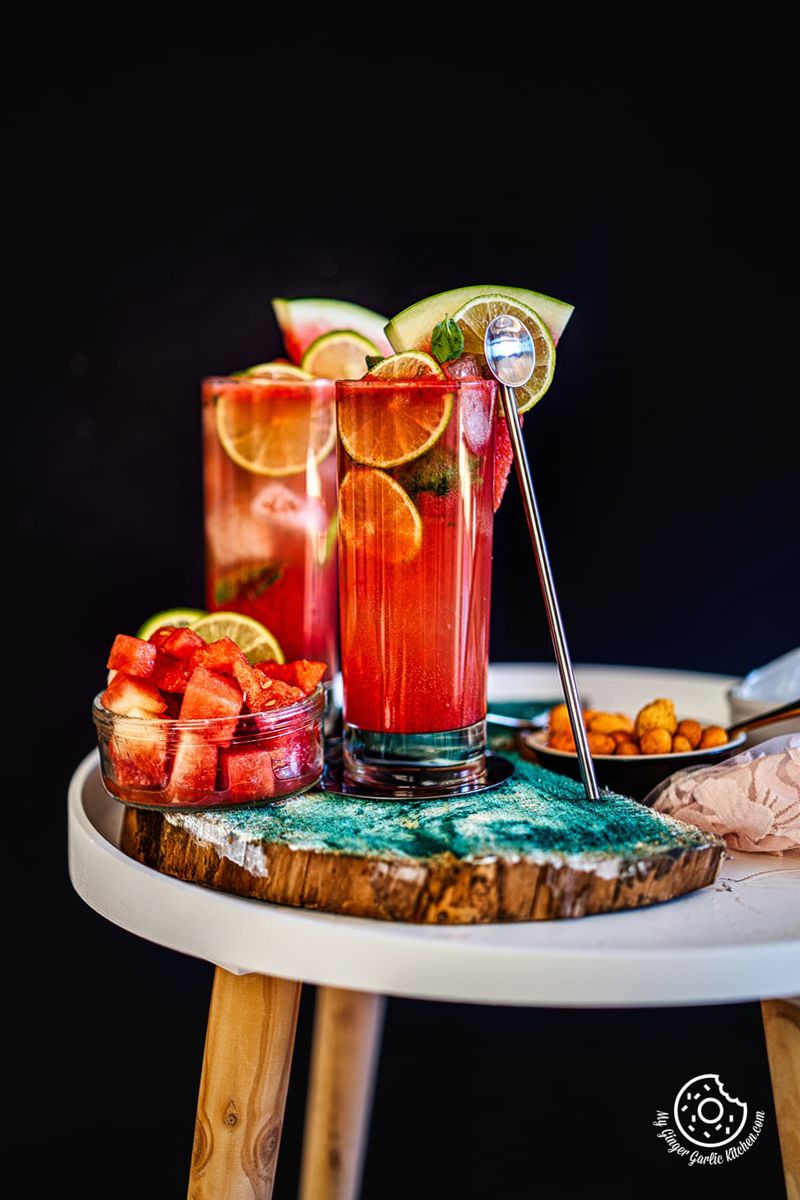 two watermelon mojito glasses kept on a white table with watermelon cubes on the side